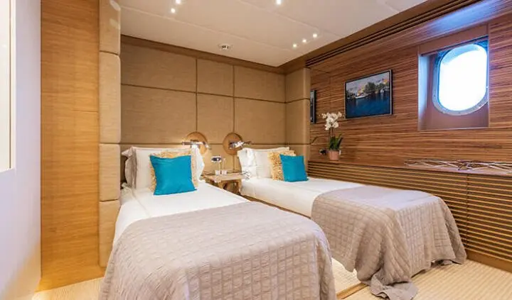 Two twin beds with beige bedding and blue pillows in a wood-paneled cabin