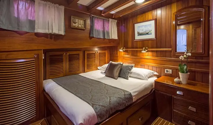Cozy master cabin with large bed, wood paneling, and overhead cabinets