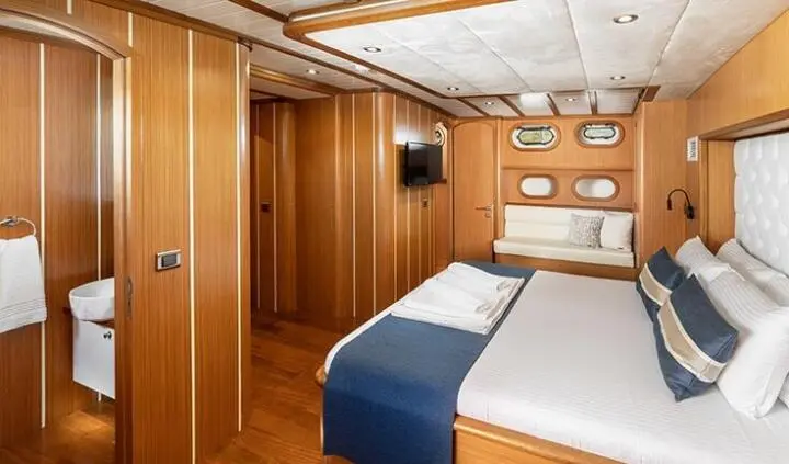 Master cabin with two single beds pushed together, wood paneling, built-in storage, and porthole windows