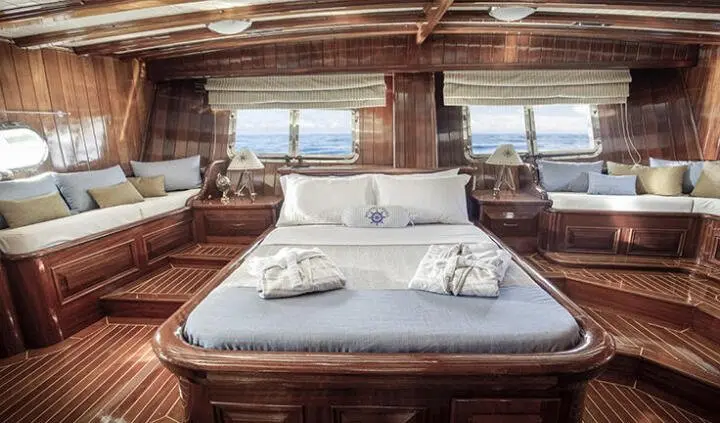 Master cabin with king bed, white linens, wooden panels, windows, and natural light