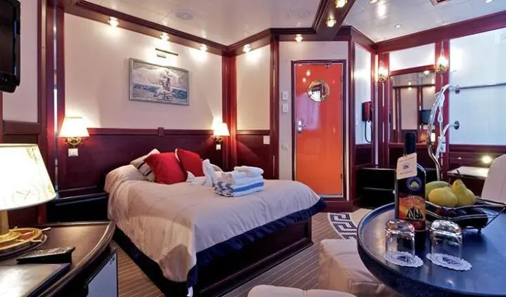 Interior view of a yacht cabin with two beds, red accents, and a doorway