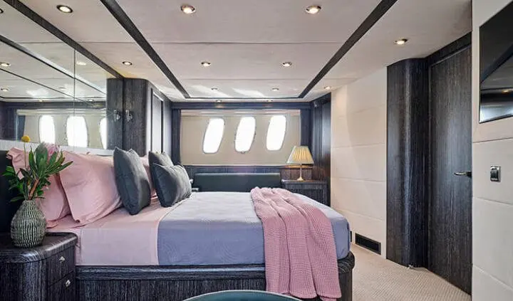 Master cabin with king bed, dark wood accents, windows, and pink blanket