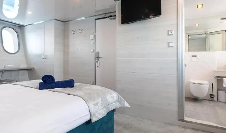 Master cabin with king bed, white walls, ensuite door, blue accents, TV mounted
