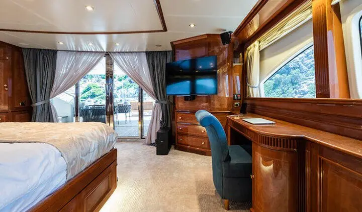 Amadea yacht cabin interior with large bed, wood paneling, work desk, and balcony doors