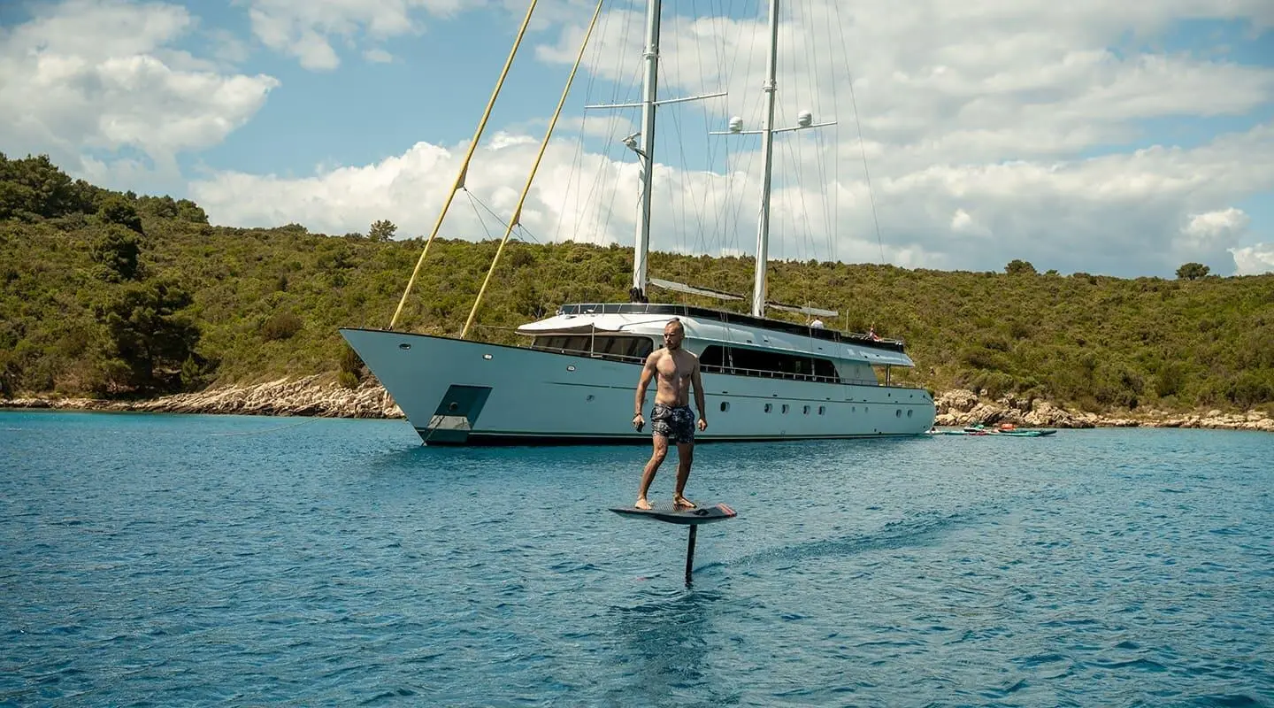 Luxury motor yacht Anima Maris anchored on calm water with person on a paddleboard nearby