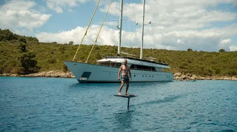 Luxury motor yacht Anima Maris anchored on calm water with person on a paddleboard nearby