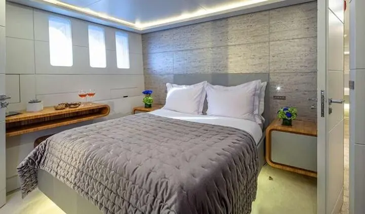 Master cabin with king bed, gray bedding, brick wall, two bedside tables, ambient lighting