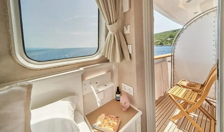 Two wooden beds in a cabin aboard La Perla yacht, with porthole view and beige curtains