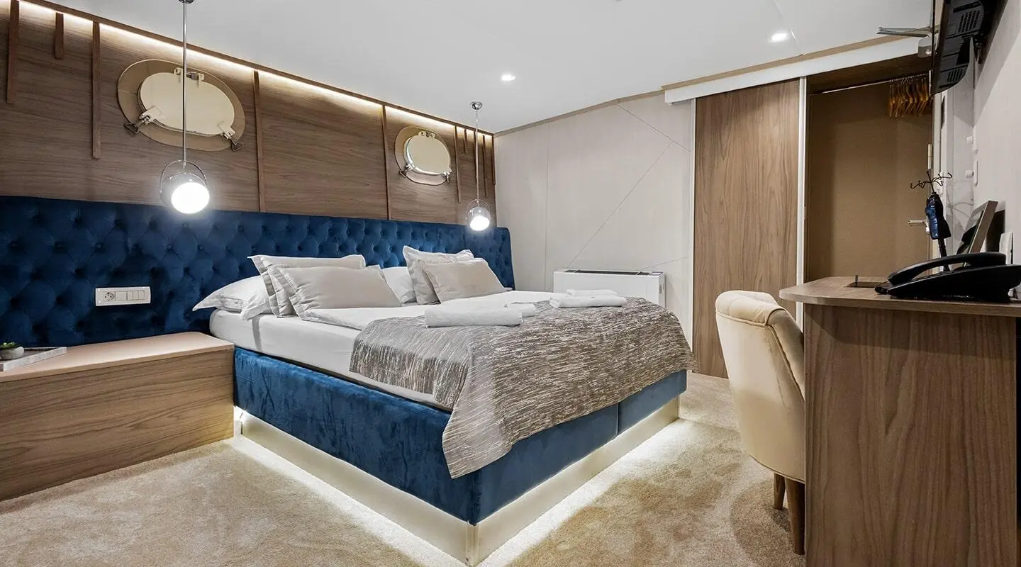 Bella yacht bedroom with blue-and-gray bedding, wooden headboard, and beige carpet