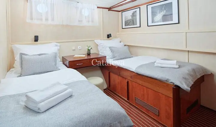 Cataleya yacht cabin with twin berths, plush white linens, grey throws, and wood accents