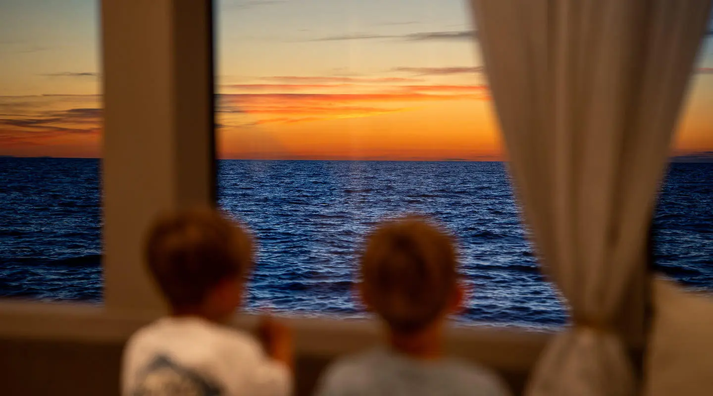 Two people watching sunset over calm sea from yacht window on Nocturno