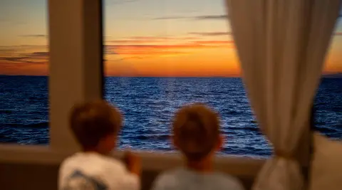 Two people watching sunset over calm sea from yacht window on Nocturno