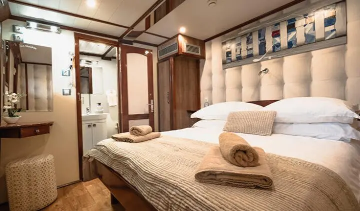 Mendula yacht cabin with double bed, beige headboard, and towels, cozy lighting