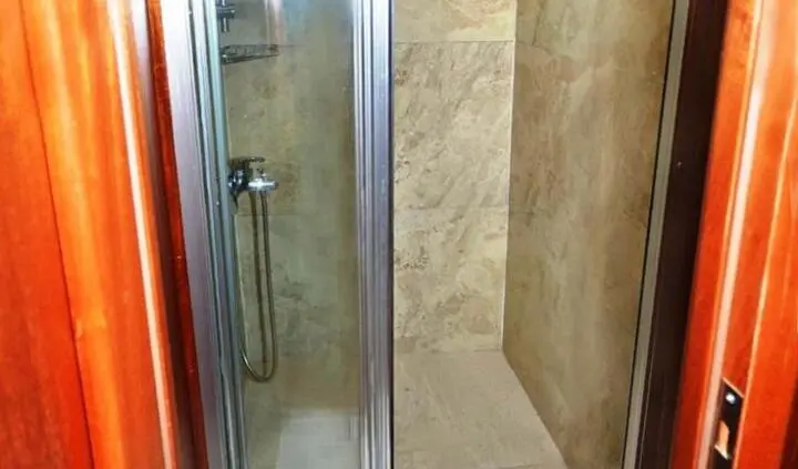 Small shower cabin with stone-patterned walls and wooden-framed doorway in a yacht cabin