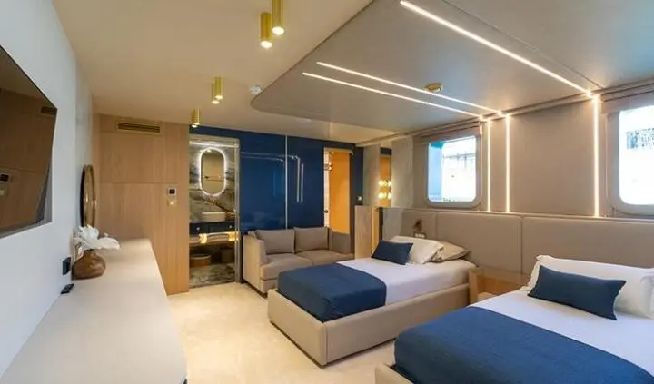 Scorpios yacht cabin with two blue beds, side windows, and seating area
