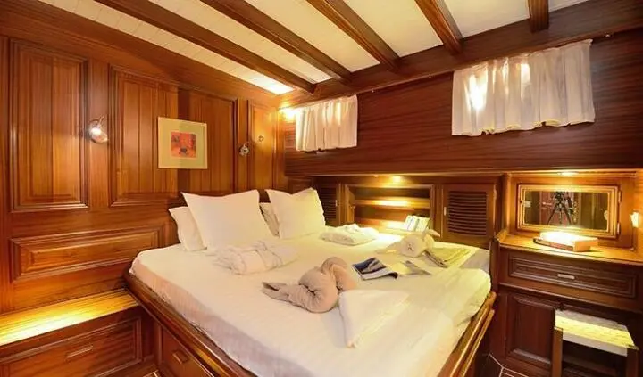 Cozy yacht cabin with a double bed, pillows, wooden beams, and warm lighting