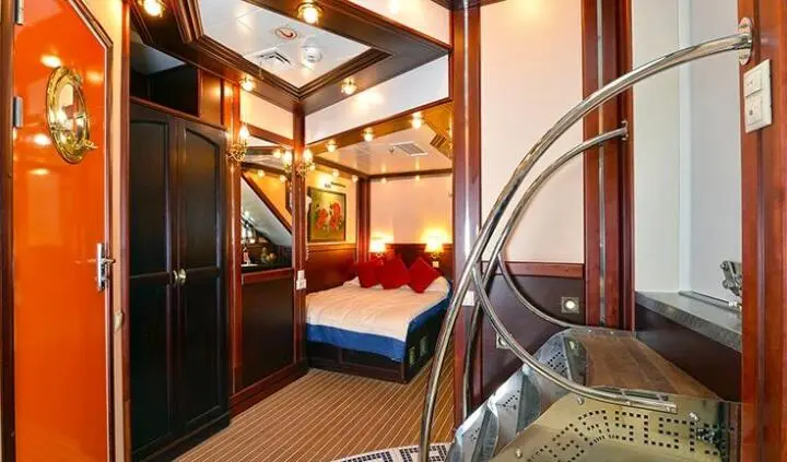 Yacht cabin interior with bed, warm lighting, wooden cabinets and stairs