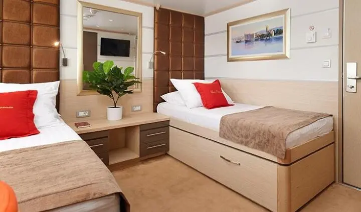 Twin cabin aboard Queen Eleganza: two single beds, plants, desk, framed art