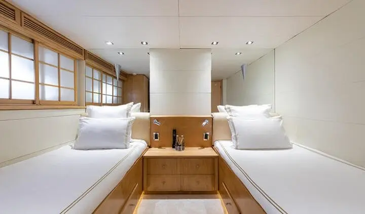 Twin cabin yacht interior with two single beds, shared wooden steps, and porthole light