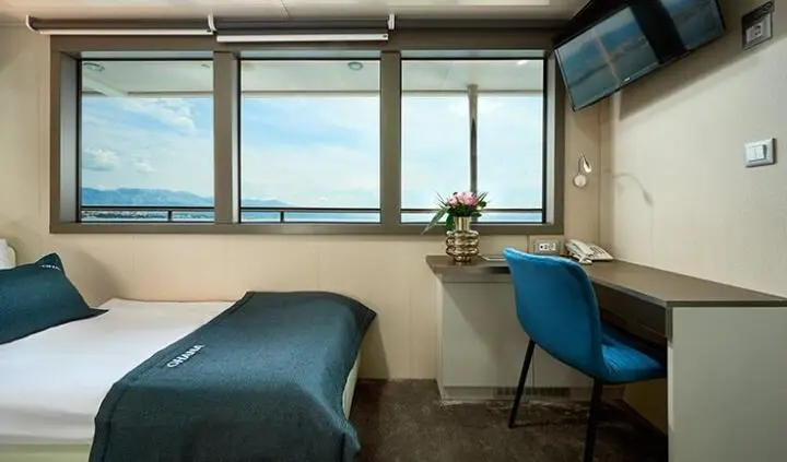 Twin cabin with two single beds, blue chair, windowed wall, sunlight