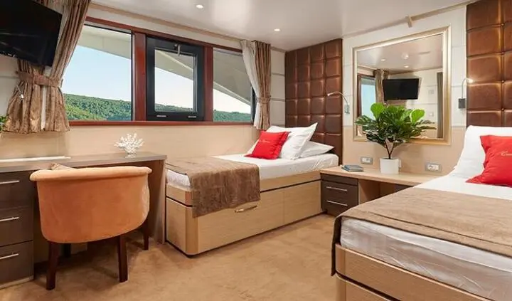Twin cabin aboard Queen Eleganza shows beige sofa, windows, and bedding