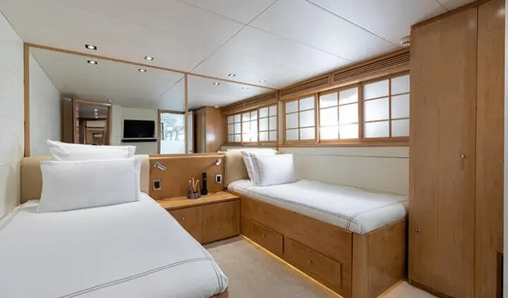 Bay-front yacht cabin with twin beds, wooden cabinets, and windows