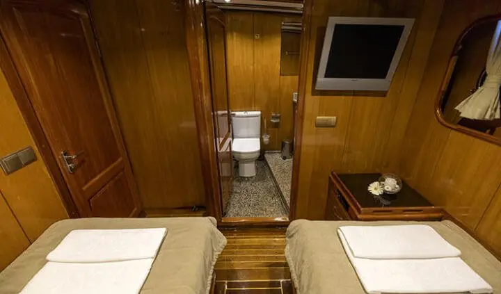 Twin-cabin luxury yacht interior with two beds, wood paneling, and small seating area