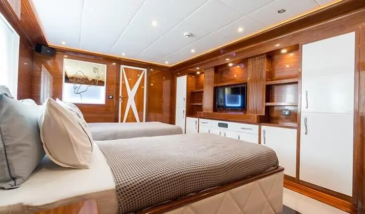 Twin cabin interior with wooden cabinetry, bed, and seating on yacht