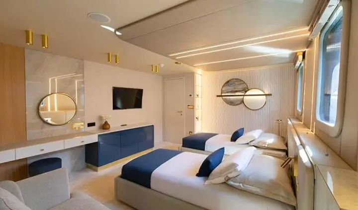 Scorpios cabin twin bed layout with blue pillows and wall-mounted TV