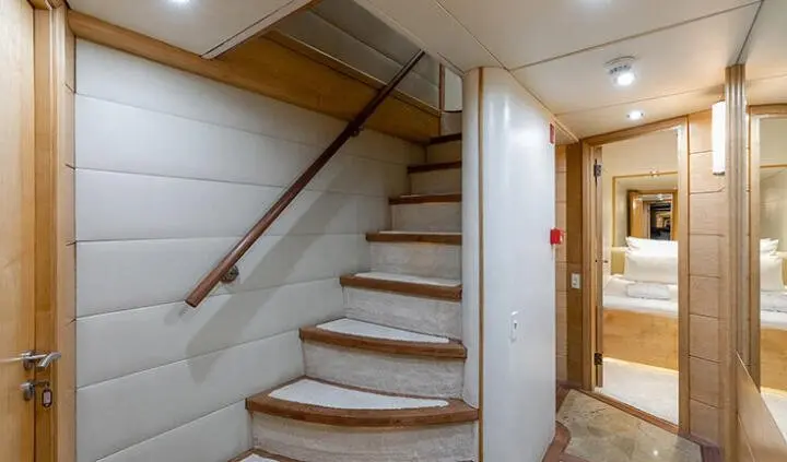 A yacht interior cabin with wooden stairs leading to upper deck and doorway