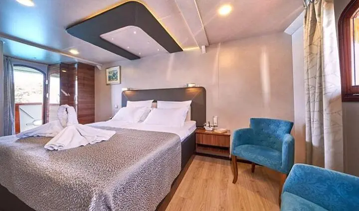Casablanca yacht cabin with two beds, bedside tables, and blue chair