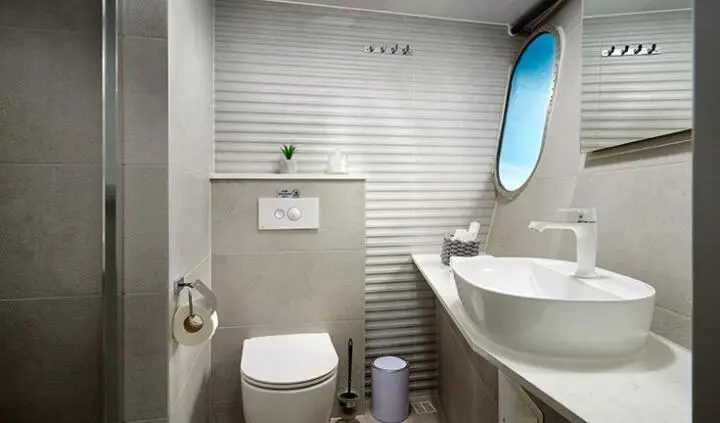 Small cabin bathroom aboard Ohana yacht, compact with toilet, sink, and striped walls