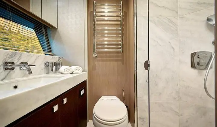 Small ensuite cabin with toilet, beige walls, wooden vanity, towel ring