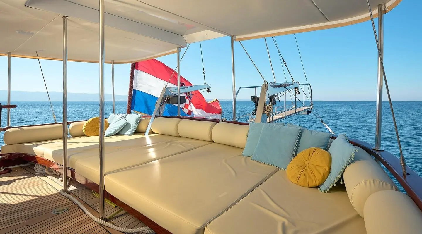 Sunlit aft deck of Linda gulet with seating, red-white-blue flag, blue sea