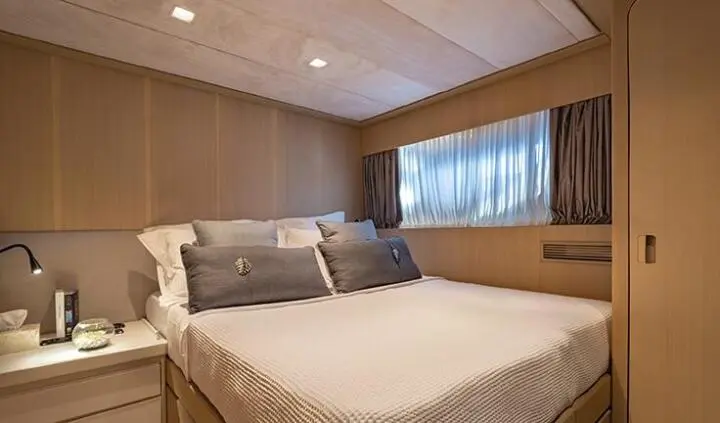 Small cabin bedroom on yacht with double bed, pillows, and window view