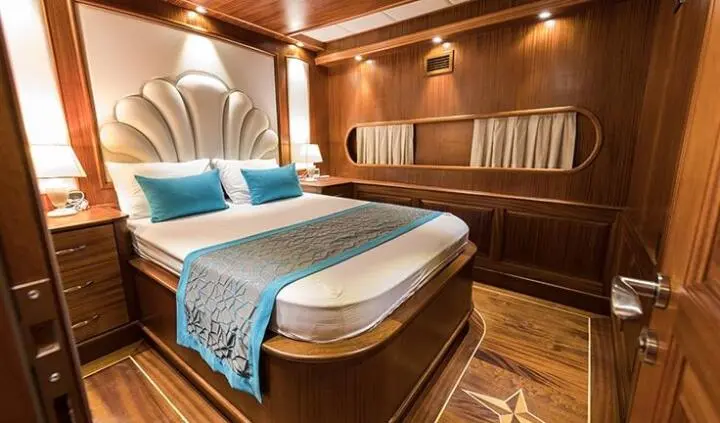 Master cabin with king bed, wooden panels, blue cushions, ensuite doorway visible