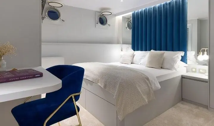 Master cabin with a large bed, white linens, blue cushions, and window with blue curtains