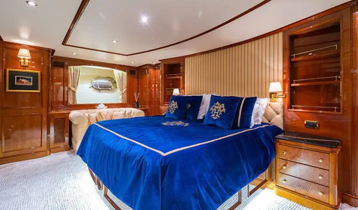Master cabin with blue bedspread, wooden cabinetry and seating area