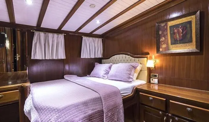 Master cabin on Grace 1 yacht with king bed, dark wood panels, and ensuite lamp