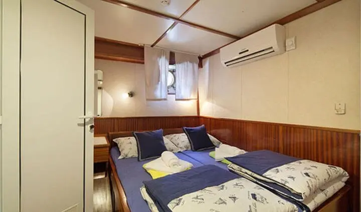 Tajna Mora yacht cabin with double bed, blue and white linens, wood paneling