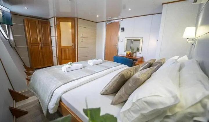 Master cabin with two single beds pushed together, white linens, brown headboard, and en-suite doorway visible