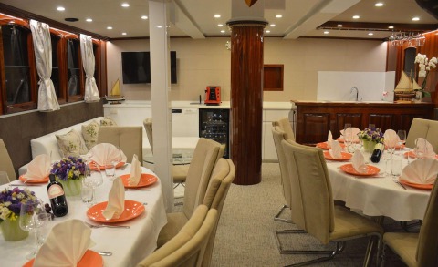 Luxurious gulet salon with dining tables and chairs, decorative flowers and a kitchenette area