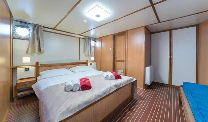 Master cabin with two single beds pushed together, wood cabinets, and striped carpet