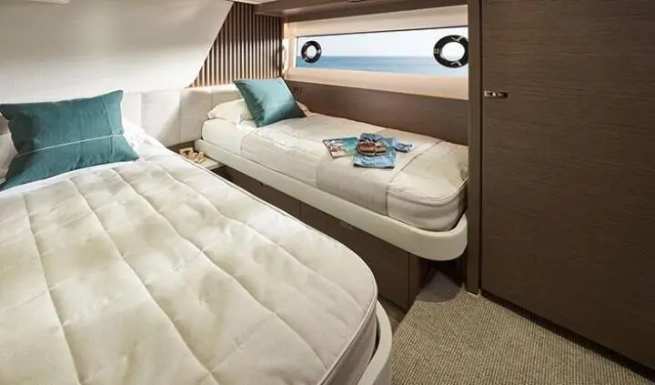 Twin cabin with bed, beige bedding, blue pillow, and port window view