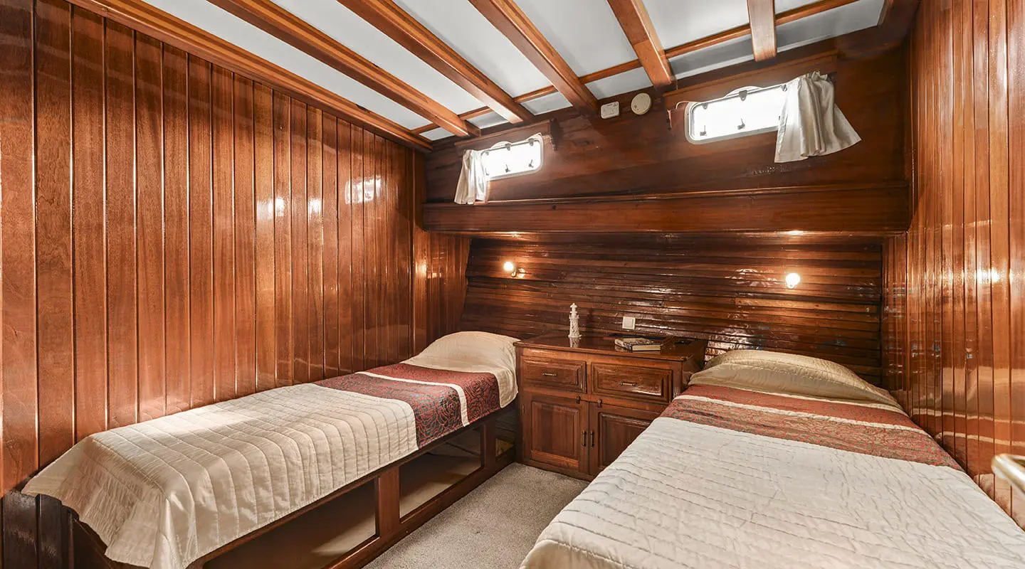 Luxurious wooden cabin interior of a yacht with two single beds and built-in desk