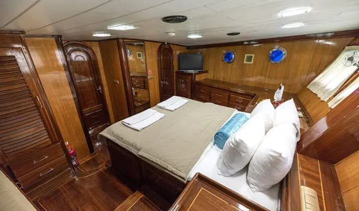 Master cabin with king bed, white linens, wooden cabinets, and porthole lighting
