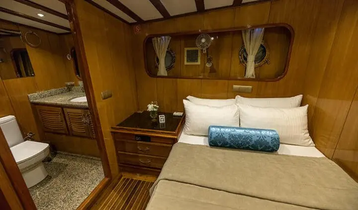 Master cabin with king bed, wooden panels, bedside table, and porthole window