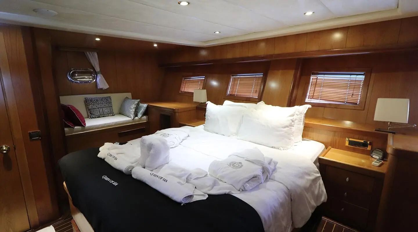 Luxurious queen-size bed with white linens inside a wood-paneled yacht cabin, soft lighting