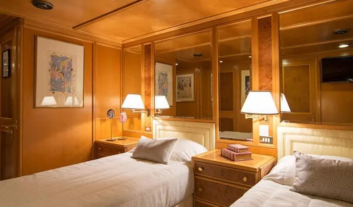Twin cabin interior with wooden paneling, two beds, bedside lamps, and a dresser
