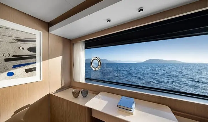 A yacht cabin with a large porthole view of the sea and a wooden desk